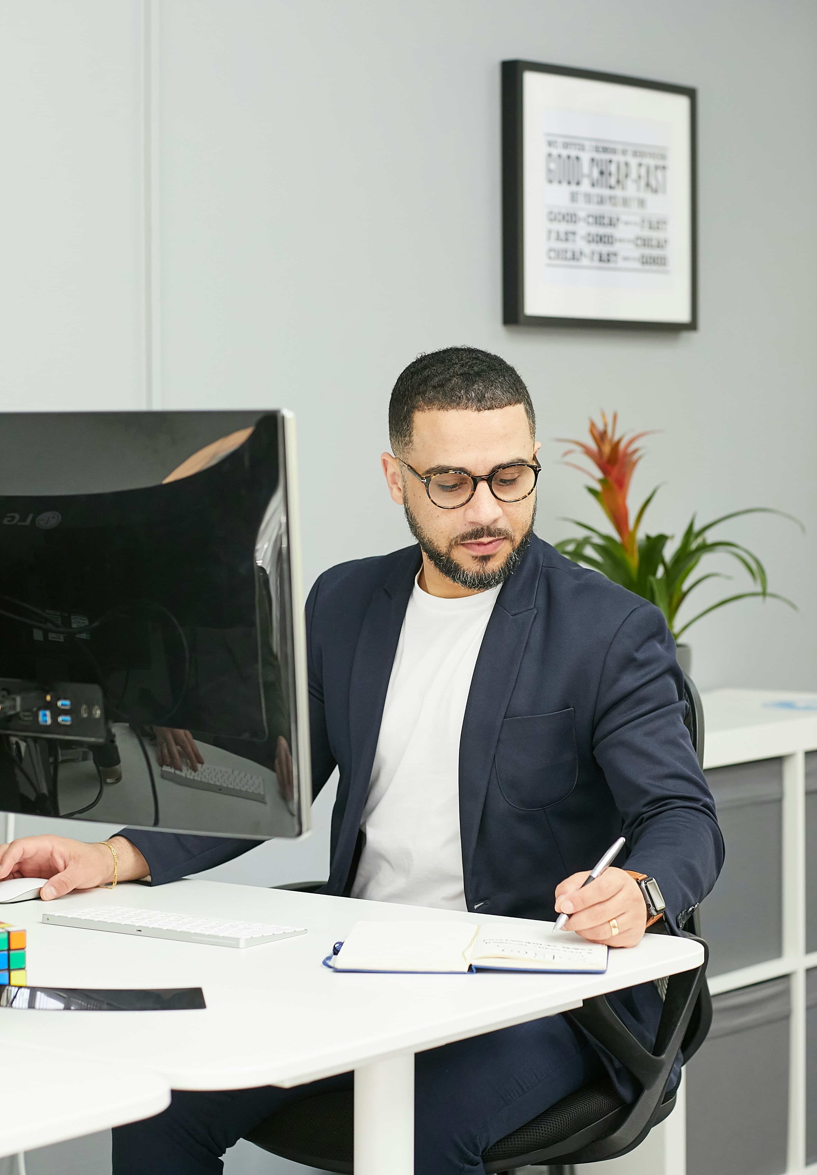 Man at computer desk writing in notebook